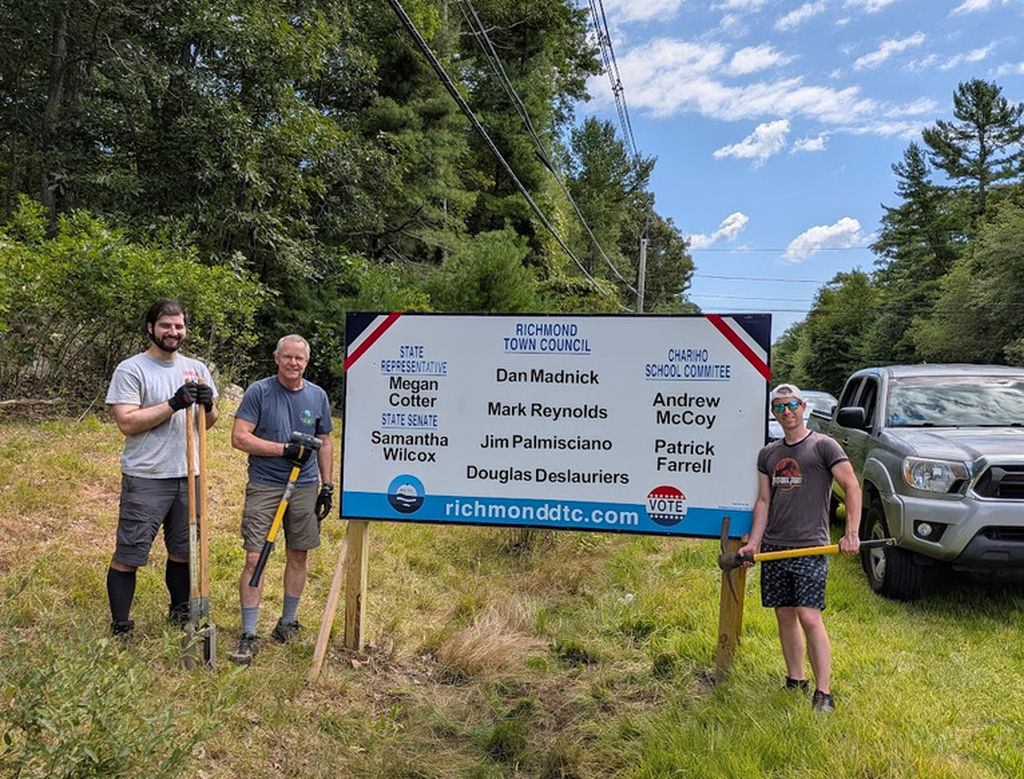 Douglas, Dan, and Patrick stand next to a large 4' by 8' sign with all RDTC endorsed names on it.