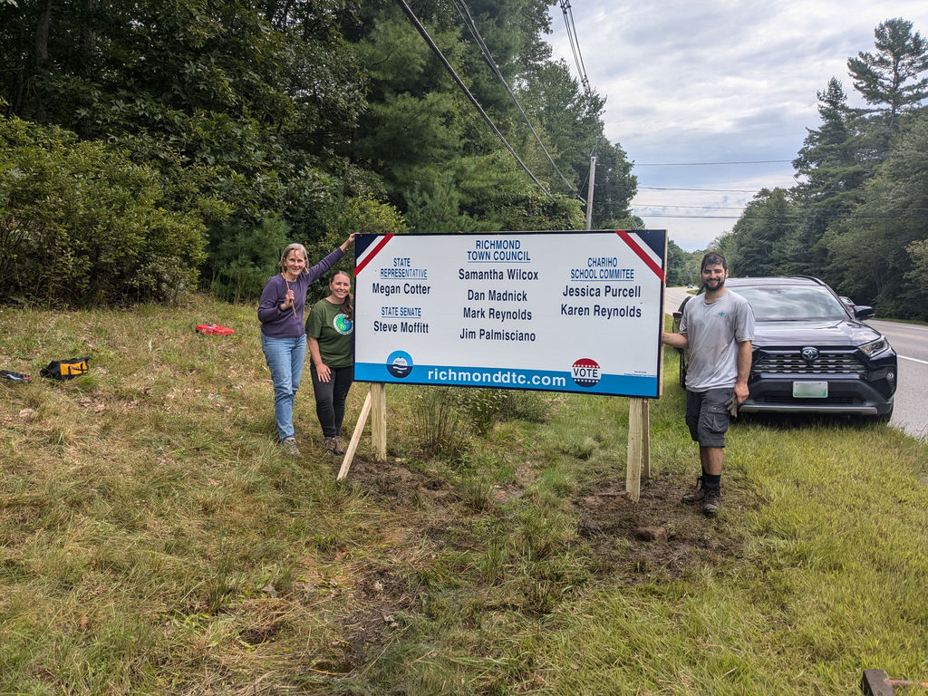 Douglas standing to the right of a large election sign in 2024