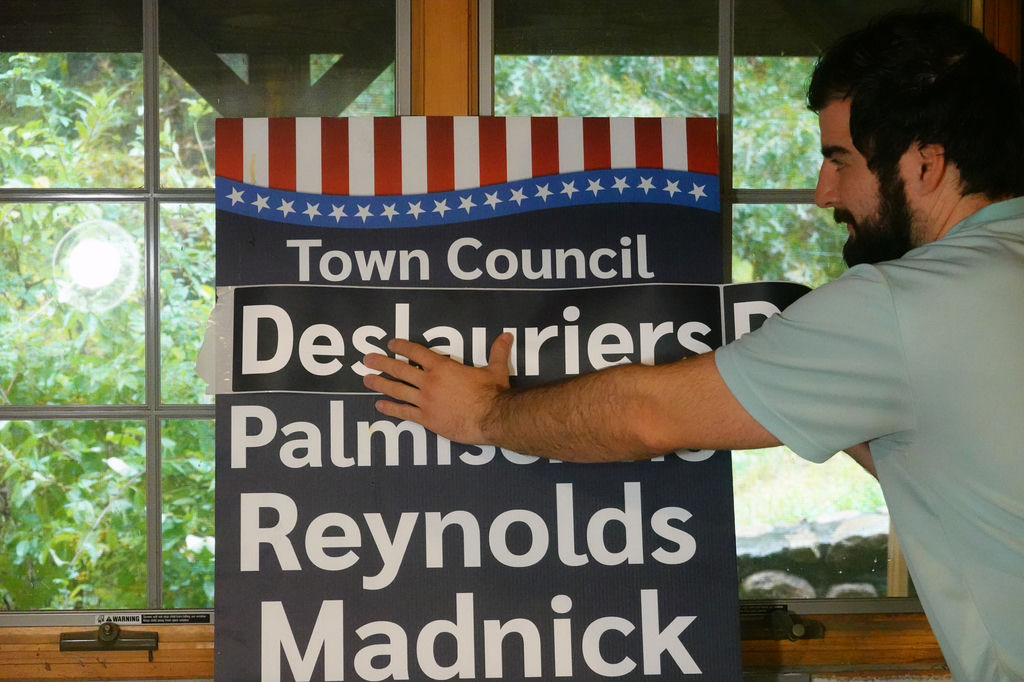 Doug applies a sticker with his last name to the existing 2024 yard sign